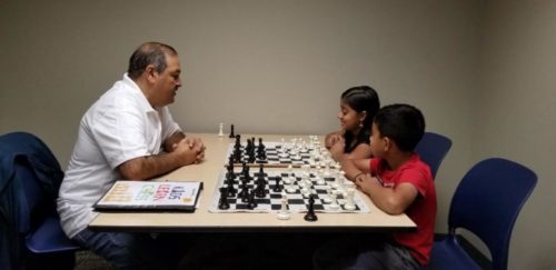 A man and two children playing chess on the table.